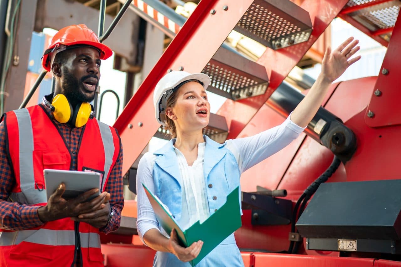 Port workers in hard hats checking paperwork beside container handling equipment